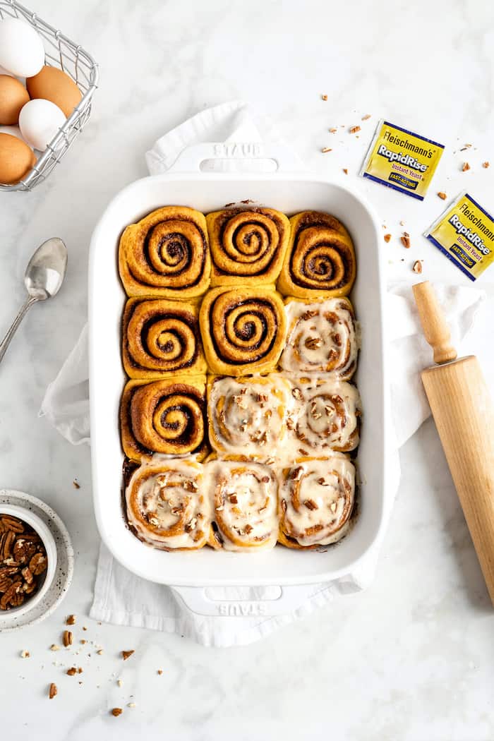 An overhead cinnamon rolls with half covered in glaze with pecans with a rolling pin