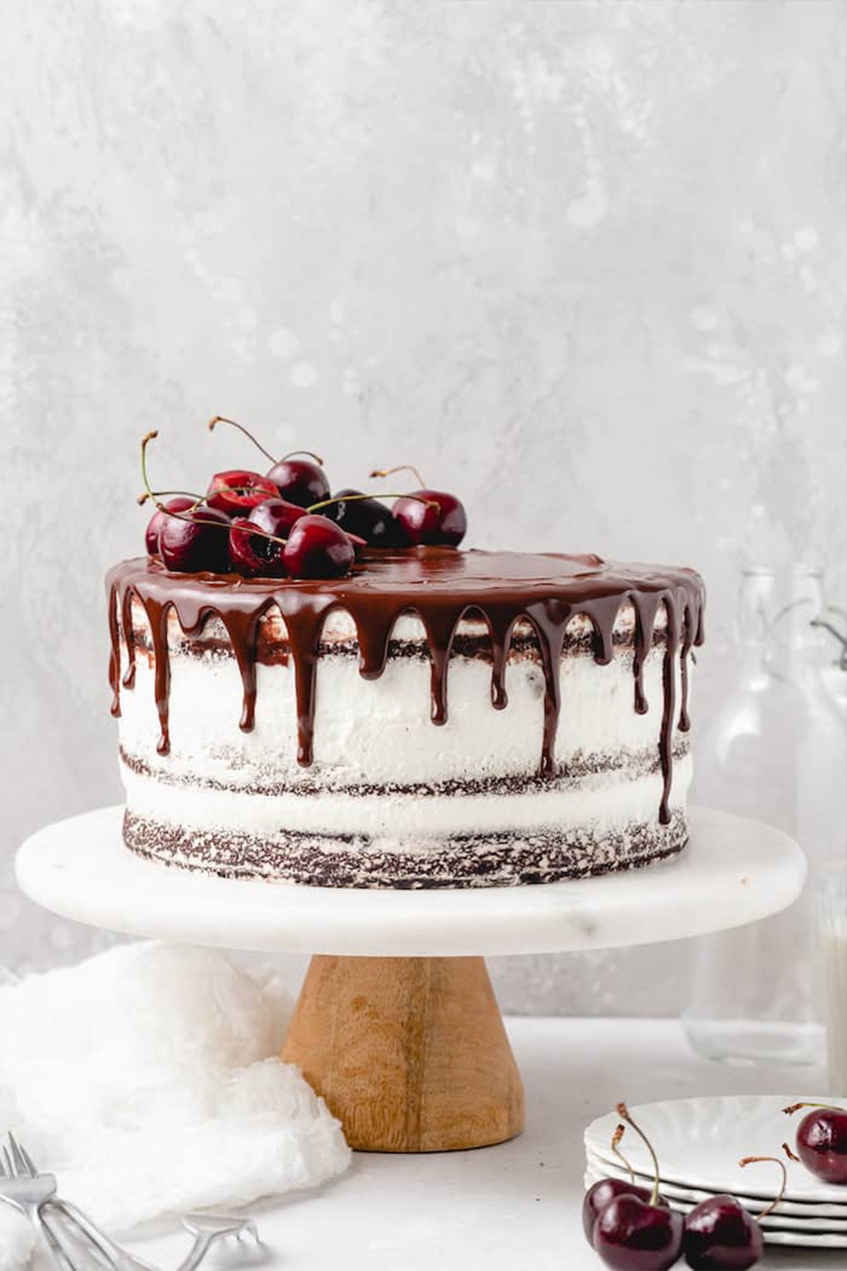 A black forest cake on a white cake stand with cherries on top against gray background.