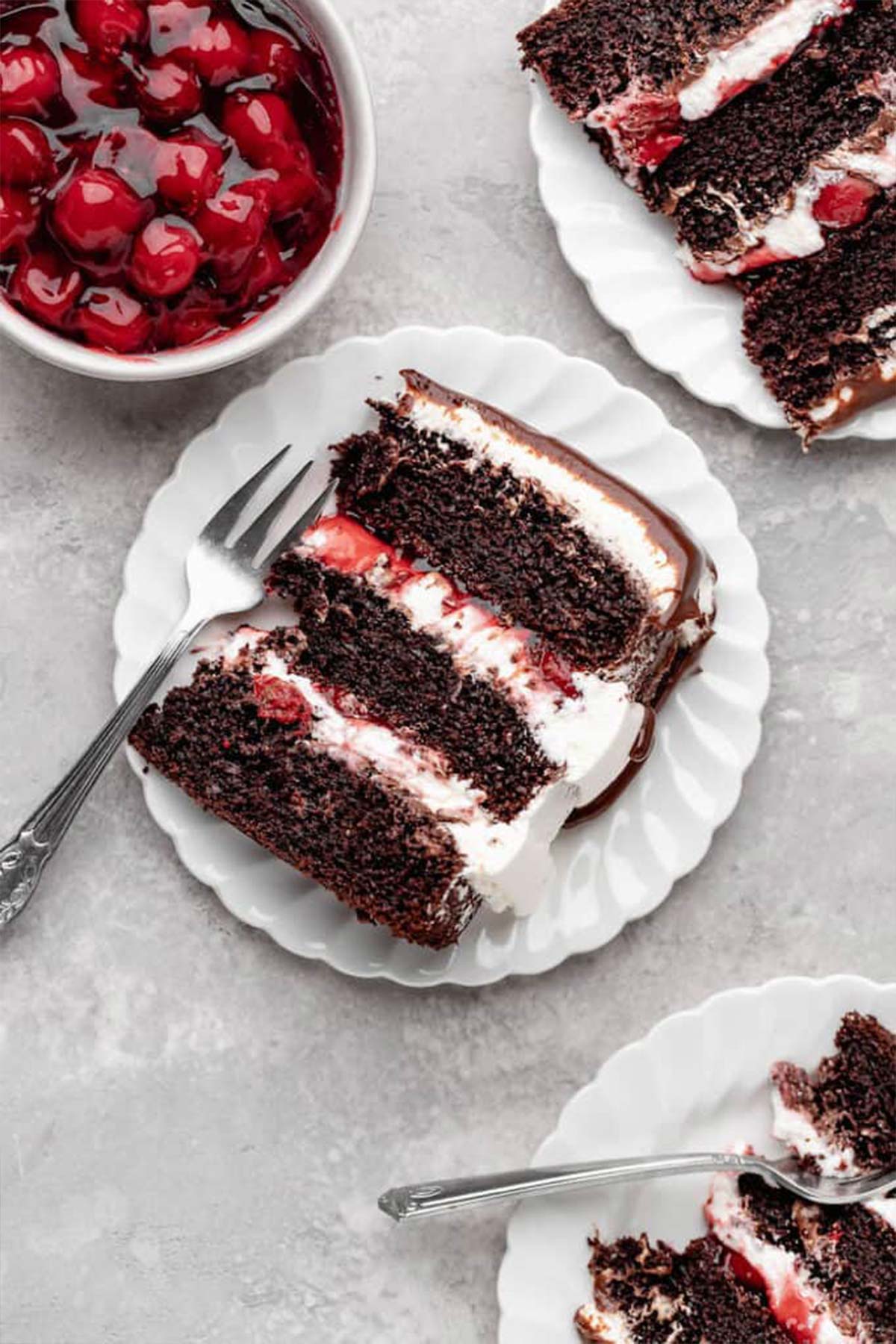 A close up of three slices of chocolate cherry filled cake with a bowl of cherry filling nearby