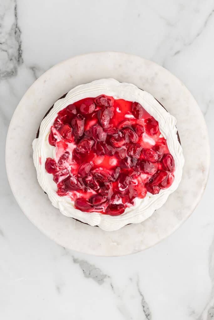 Whipped cream and cherry filling added to a forest cake.