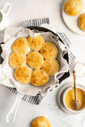 Baked angel biscuits in a round baking dish after coming out of the oven with honey nearby