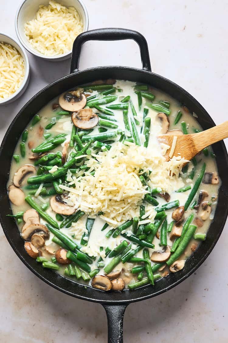 Shredded cheese mixing into a filling of green beans and mushrooms