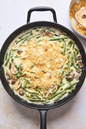 A creamy cheesy green bean filling in a cast iron skillet with panko crumbs tossed on top