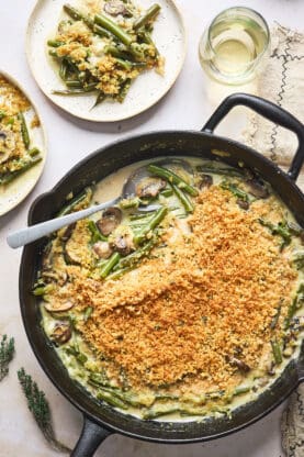 An overhead of a green bean casserole with a spoon serving some on two white plates