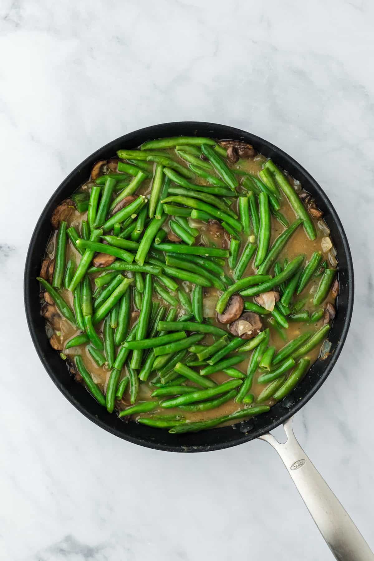 Green beans added to a skillet to cook in a white wine chicken stock sauce