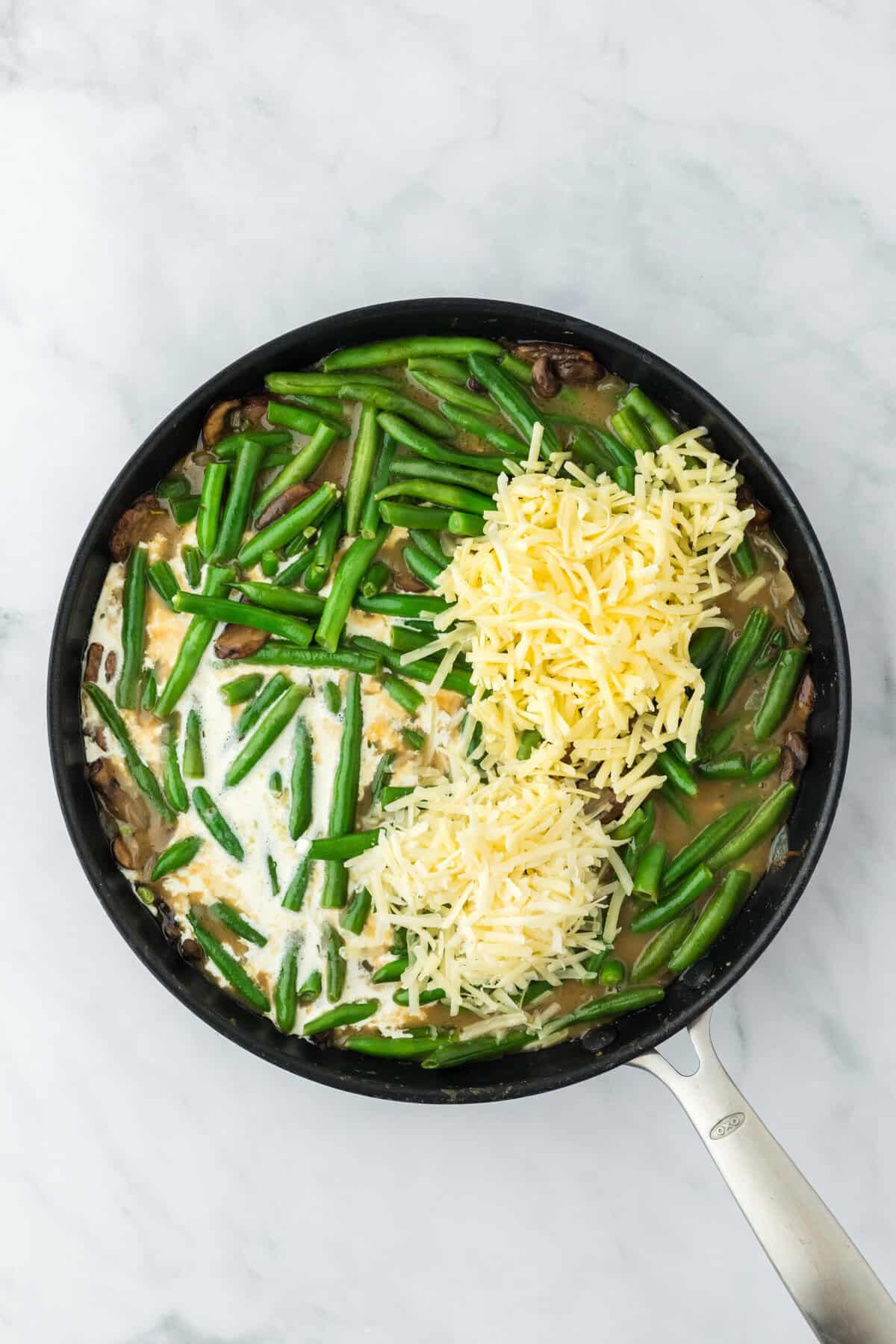 Gruyere and cheddar being added to a homemade green bean casserole on the skillet