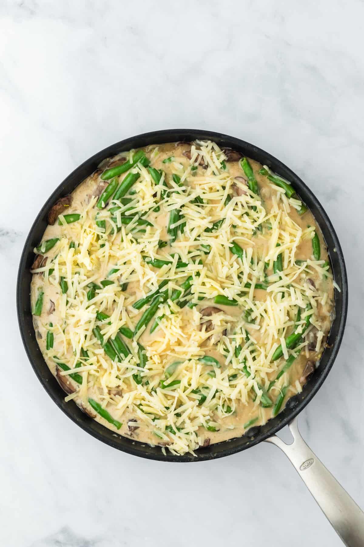 Shredded cheeses added to top of easy green bean casserole recipe before baking