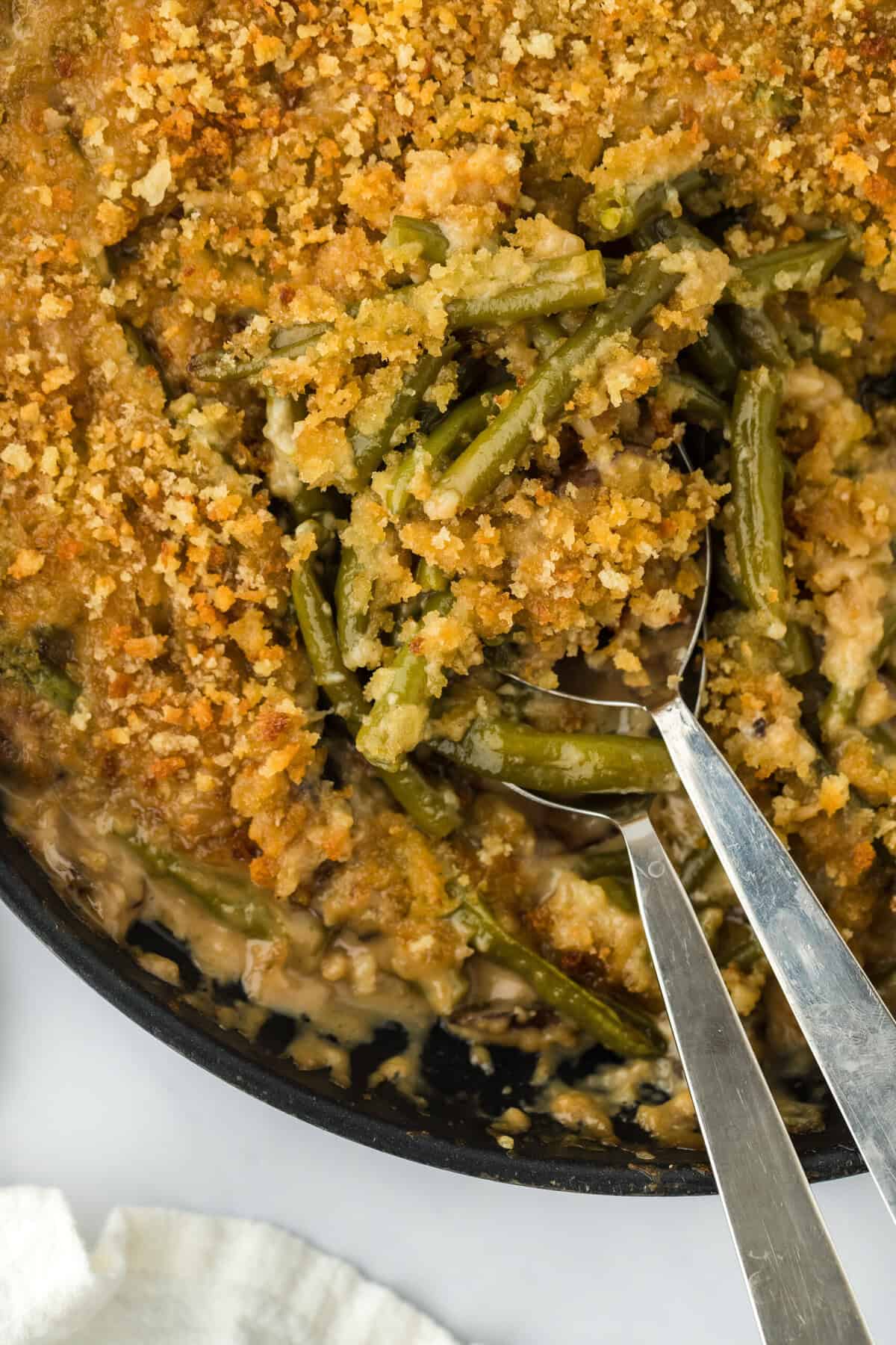 The best green bean casserole being dug into with two spoons on white background