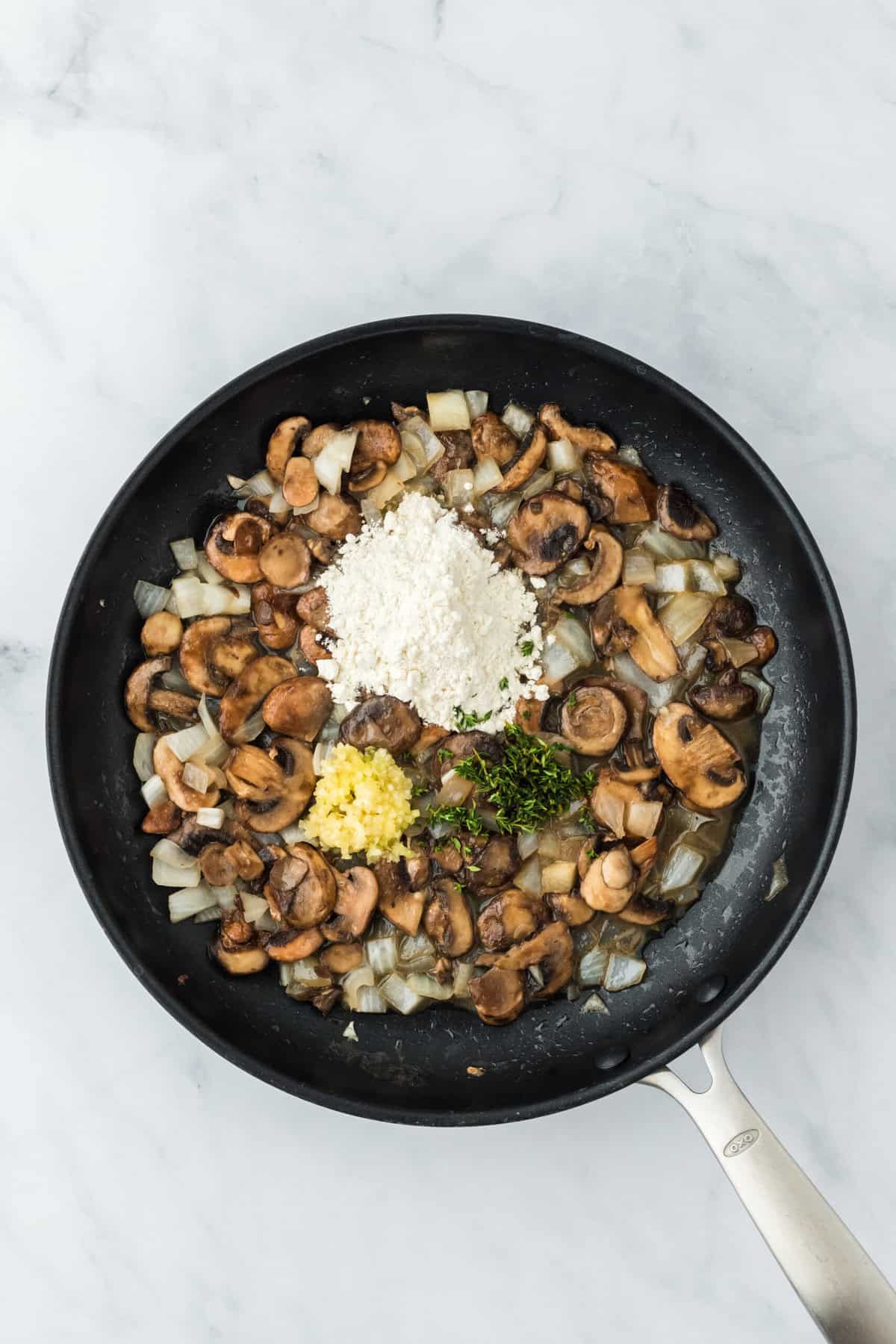 Garlic, thyme and flour added to mushroom and onion butter mix in a large skillet