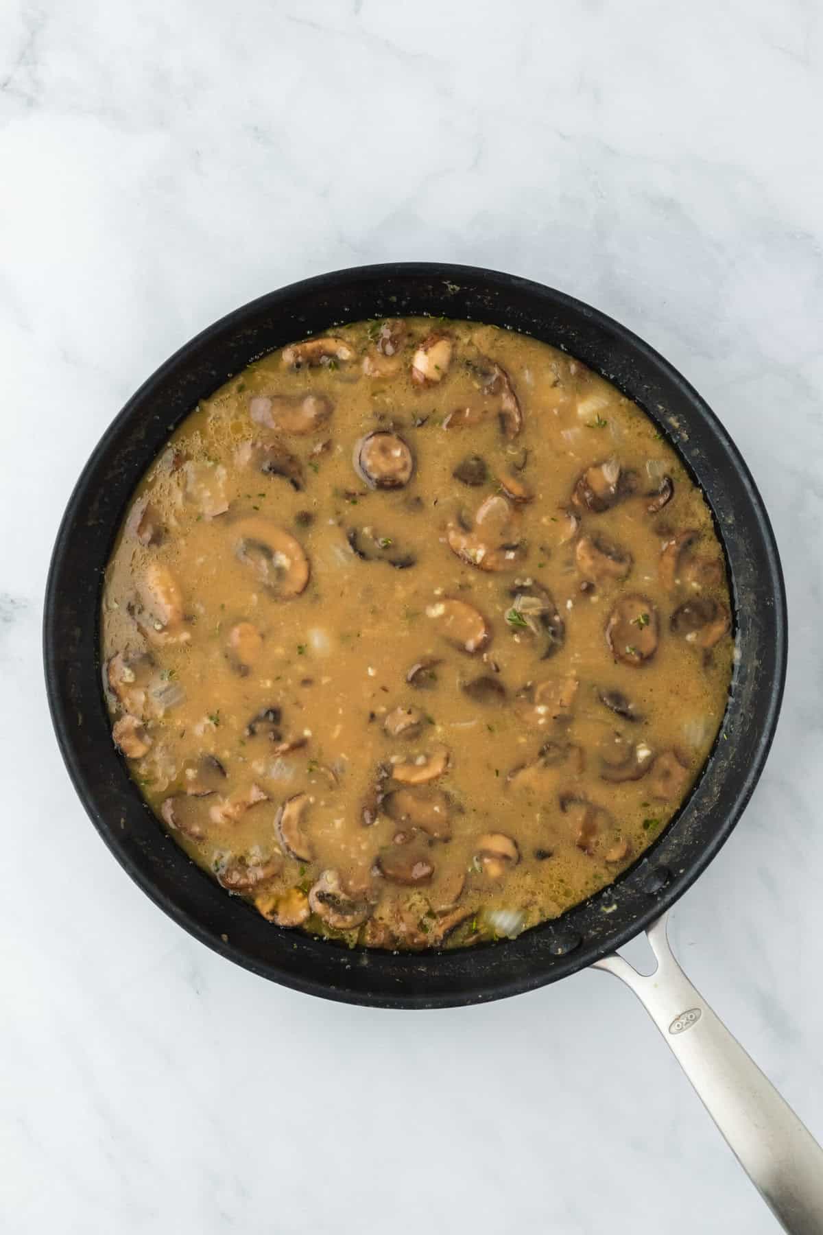 White wine and chicken stock sauce with mushrooms and onions cooking away in skillet