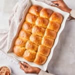 Black female hands holding a white dish of dinner rolls after baking