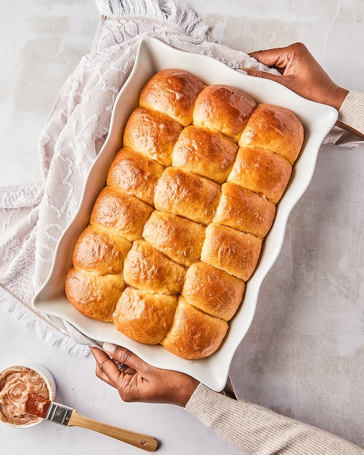 Black female hands holding a white dish of dinner rolls after baking