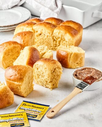 Honey butter dinner rolls against white background with honey butter and a brush nearby