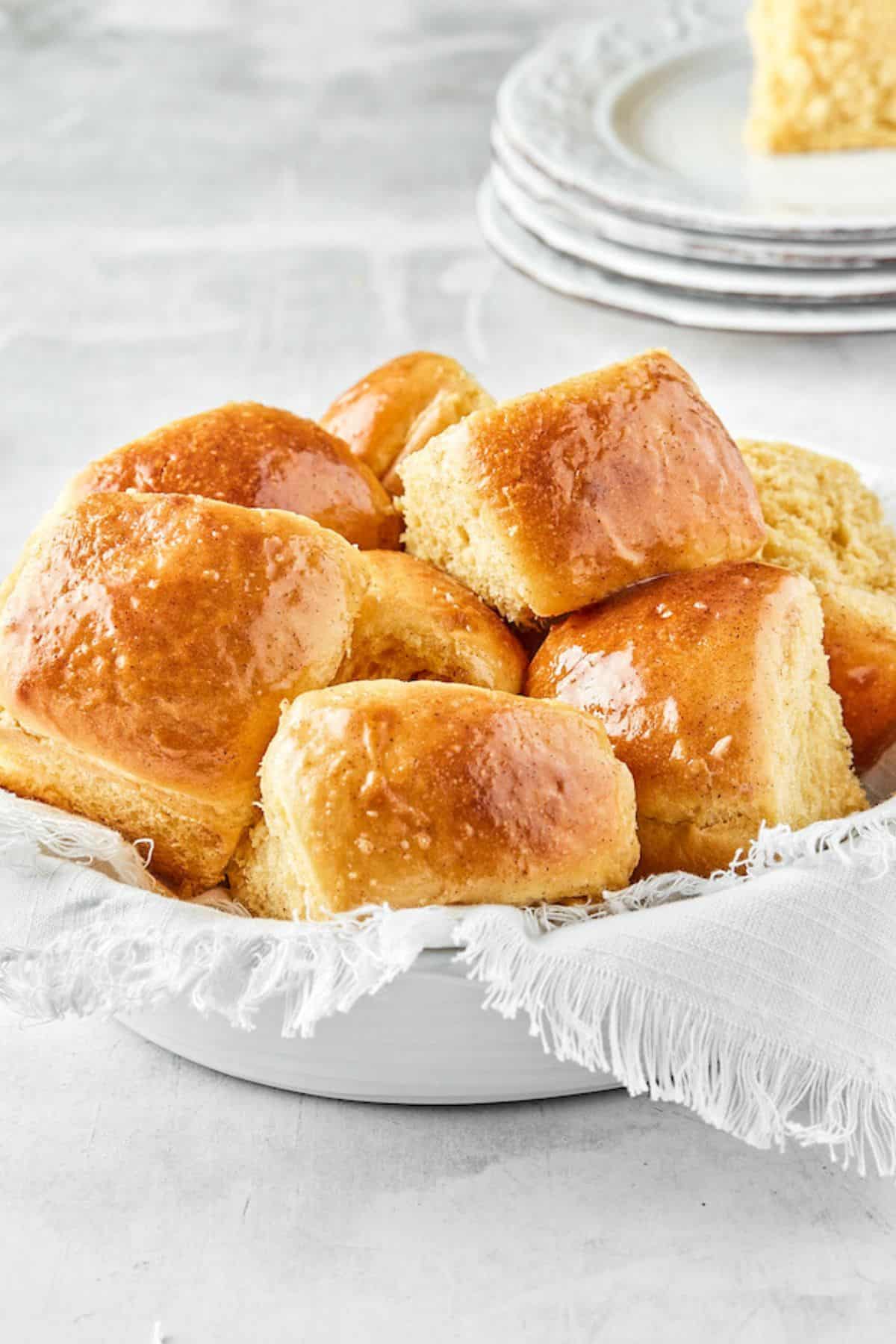 Honey butter dinner rolls in a bowl lined with a white cloth, stacked and ready to serve, showing a glossy finish