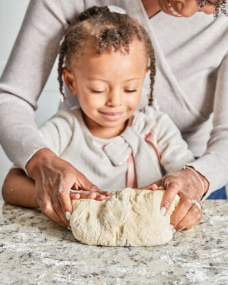 A black little girl helping mother knead dinner roll dough