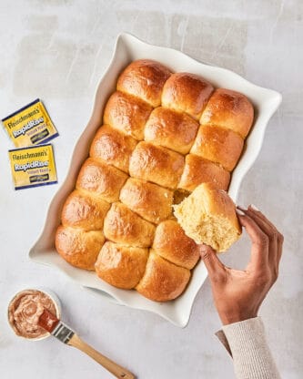 Honey butter dinner rolls after baking with a black female hand holding one with packs of yeast in the background