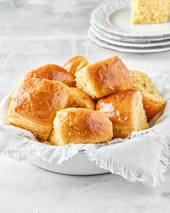 Honey butter dinner rolls in a white bowl against a white napkin after baking