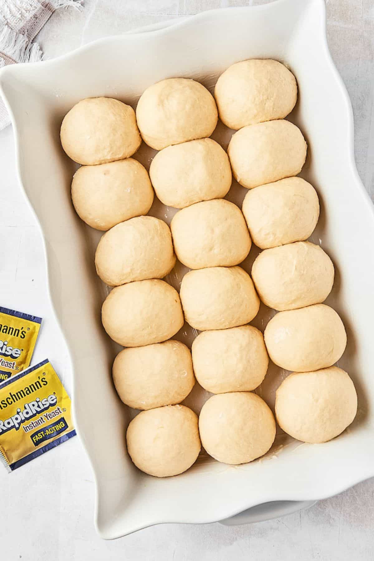 A baking dish filled with risen dough balls ready to be baked, with packets of yeast nearby