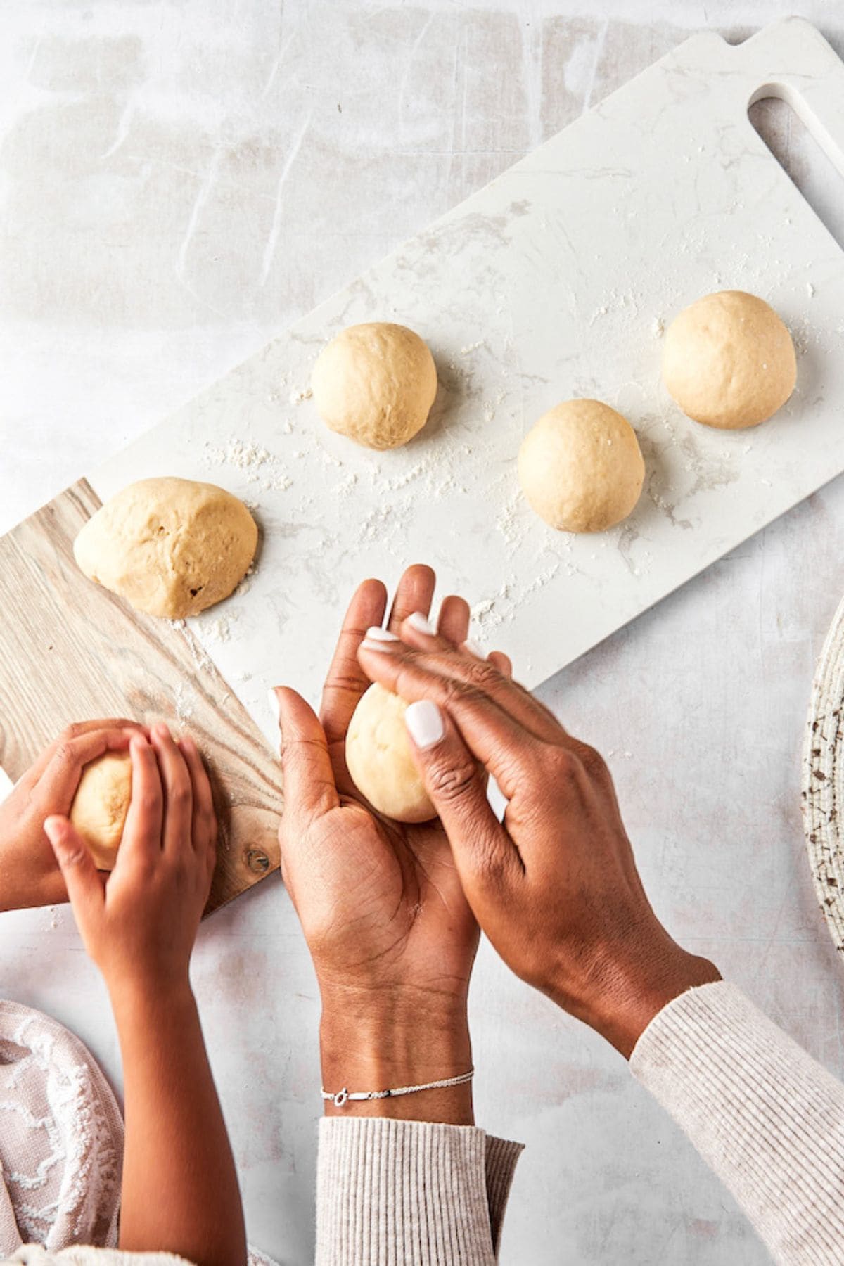 Hands of an adult and child shaping dough balls on a lightly floured surface