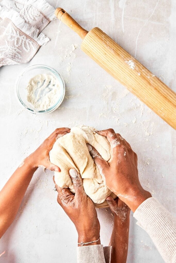 Adult and child hands kneading dough together on a flour-dusted countertop