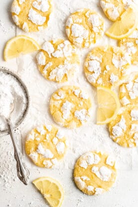 Lemon crinkle cookies scattered against a white background with powdered sugar nearby