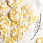 Lemon sugar cookies that are piled up on white parchment paper with wedges of lemon near them