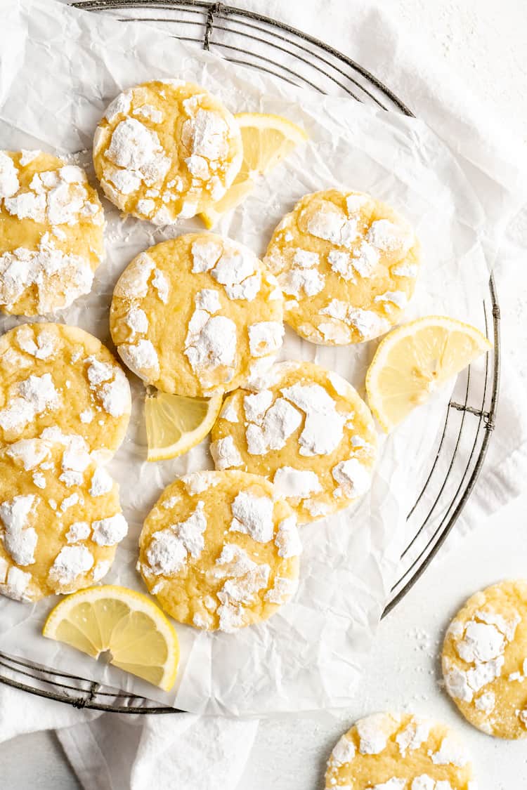 Lemon sugar cookies that are piled up on white parchment paper with wedges of lemon near them