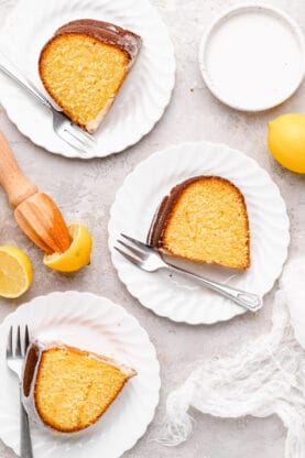 An overhead of several slices of olive oil cake on white plates with lemons nearby
