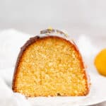 A slice of lemon olive oil cake on a white plate with a white napkin in the background