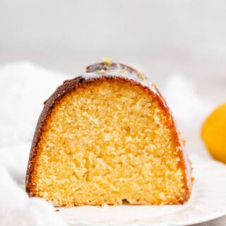 A slice of lemon olive oil cake on a white plate with a white napkin in the background