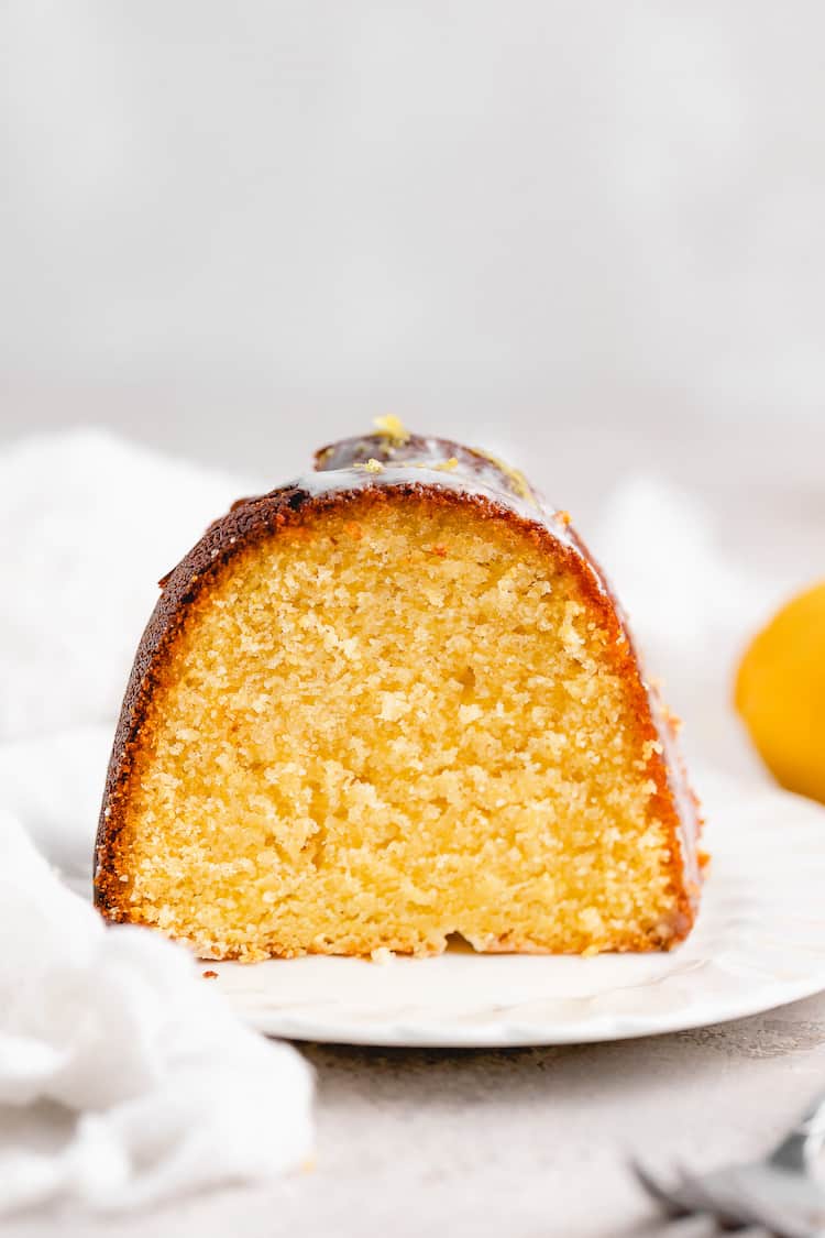 A slice of lemon olive oil cake on a white plate with a white napkin in the background