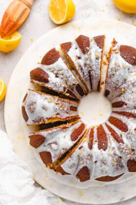 An overhead of a large lemon bundt cake that has been sliced with zested lemon on top