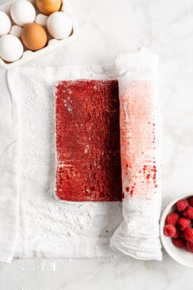 A red velvet jelly roll being rolled up against parchment paper