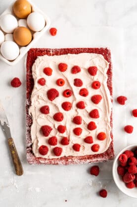 Raspberry buttercream spread over a thin layer of red velvet sheet cake with raspberries on top