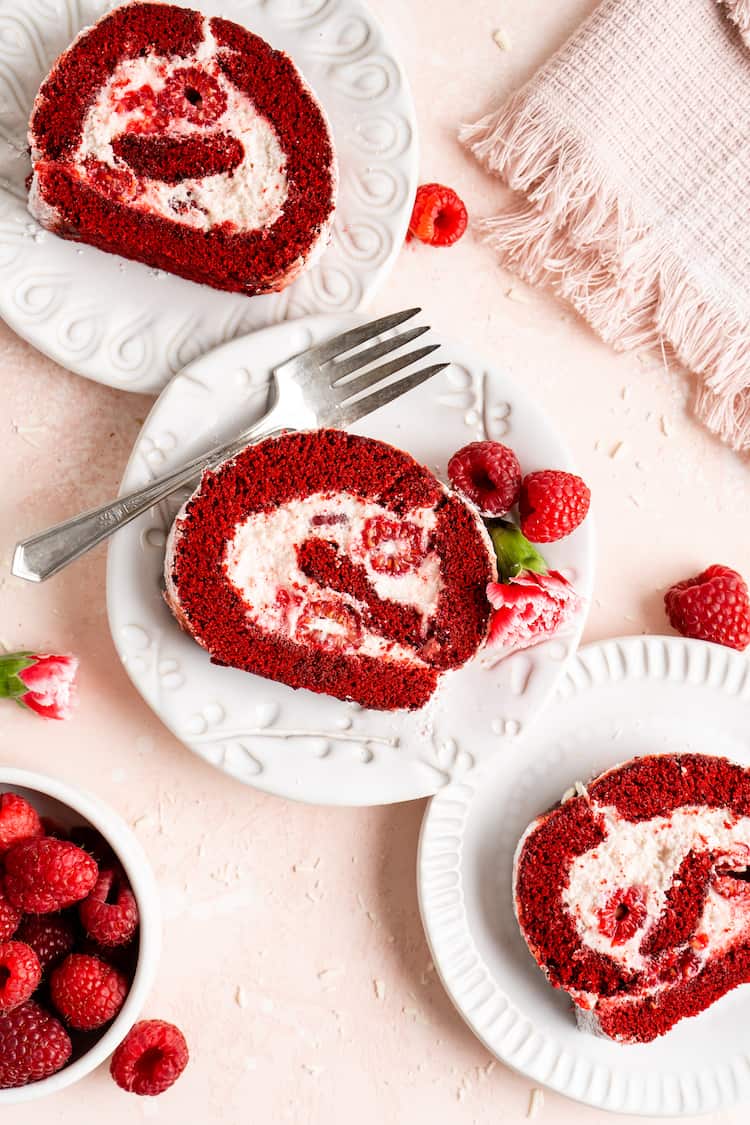 Slices of red velvet cake roll on three white plates with a silver fork