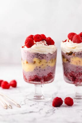 Two red velvet trifles with raspberries on top and raspberries in the background