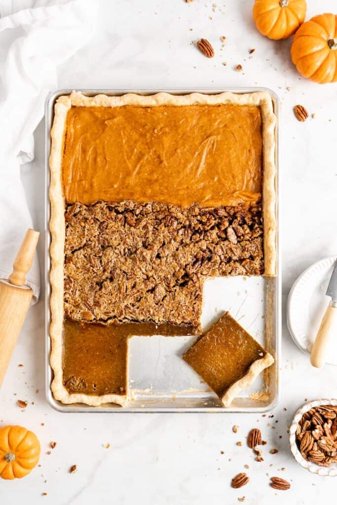 An overhead shot of a sheet pan pie baked with sweet potato pie, pecan pie and pumpkin pie fillings against a white background with a few slices cut to serve