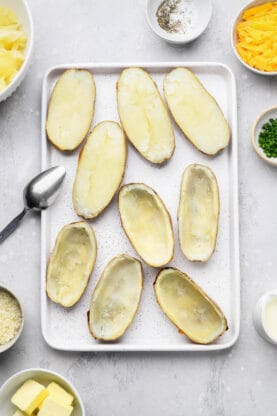 Sliced baked potatoes with filling scooped out on baking sheet
