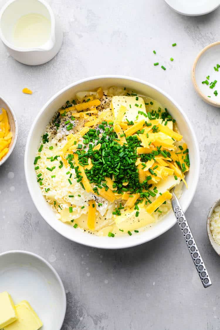 Potato filling in a white bowl with chives, butter and cheddar cheese before mixing together