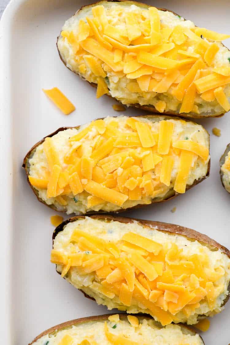 A close up of twice baked potatoes with shredded cheese before baking