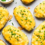 Twice baked potatoes on a gray surface with chives on top after melting