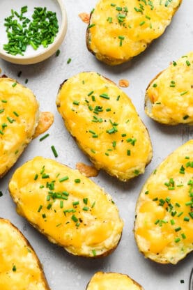 Twice baked potatoes on a gray surface with chives on top after melting