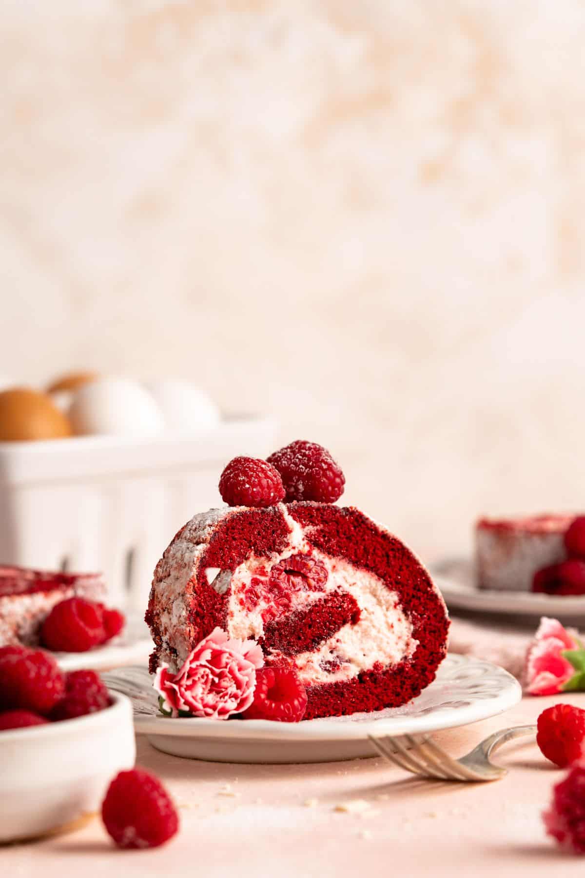 A straight on look at a slice of red velvet cake roll piled high with raspberries