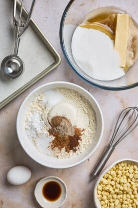 Dry ingredients for baking cookies in a white bowl with additional white chocolate chips nearby as well