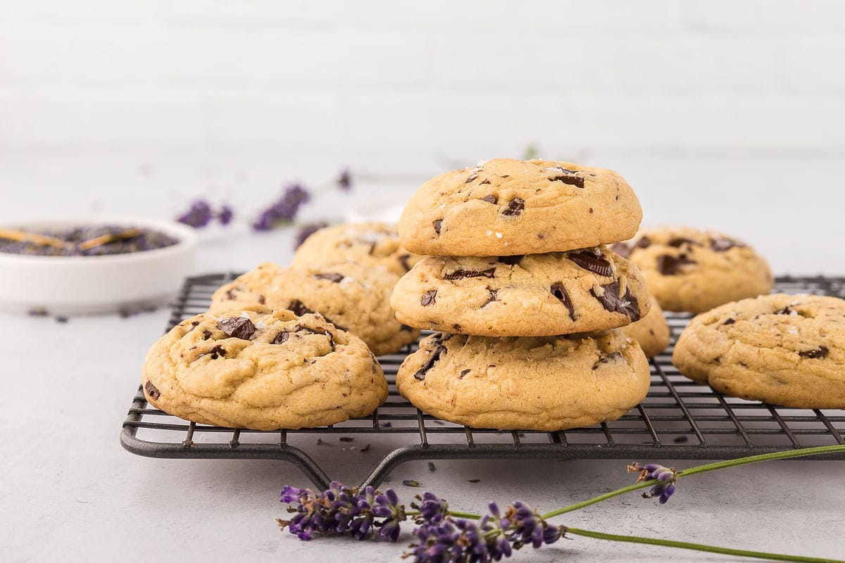 Chocolate chip lavender cookies on a wire rack with three stacked on top in the front.