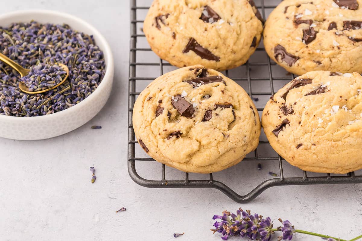 Lavender chocolate chip cookies cooling on a rack with a bowl of lavender with a spoon next to it.