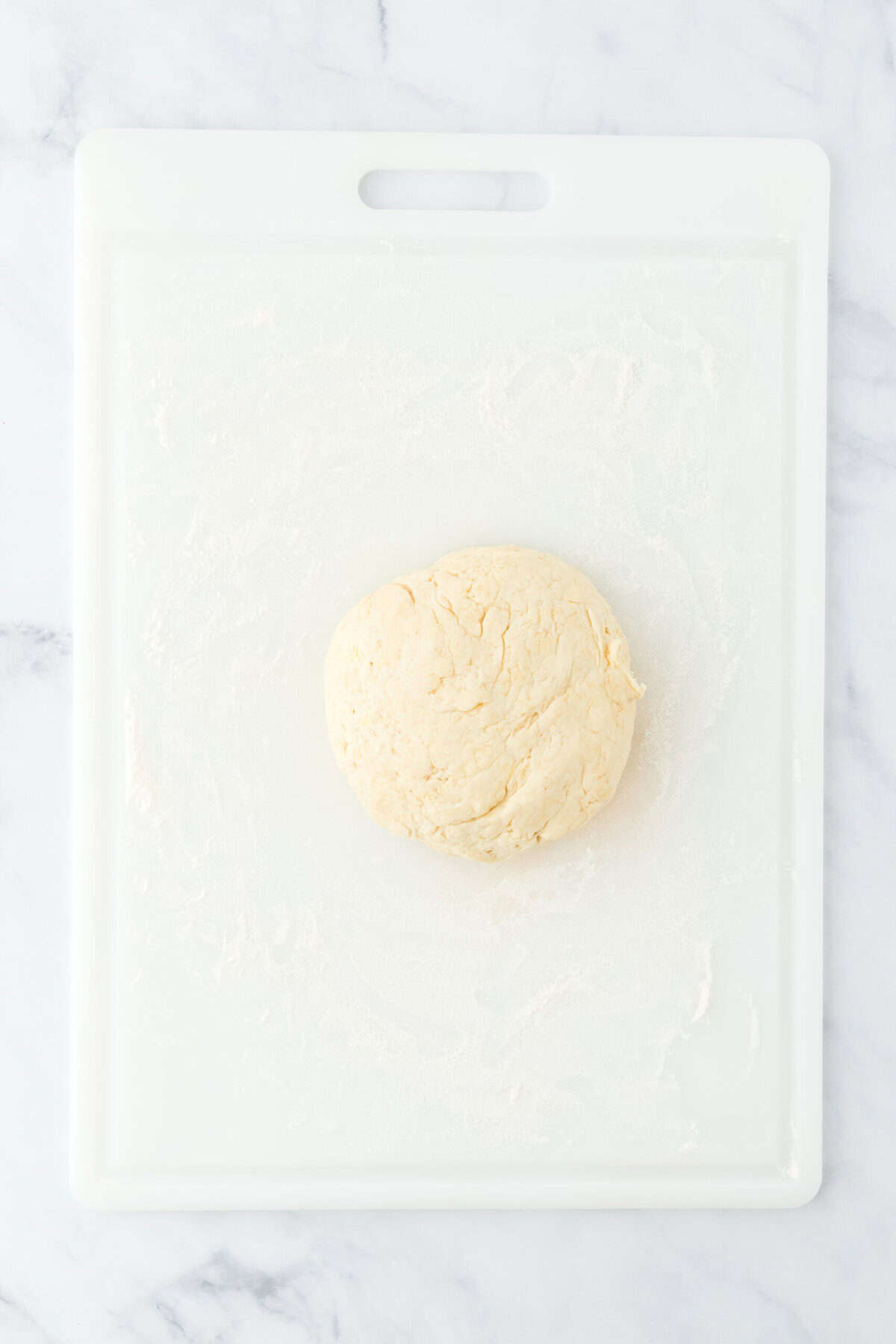 Southern angel biscuit dough kneaded on a floured work surface on white countertop