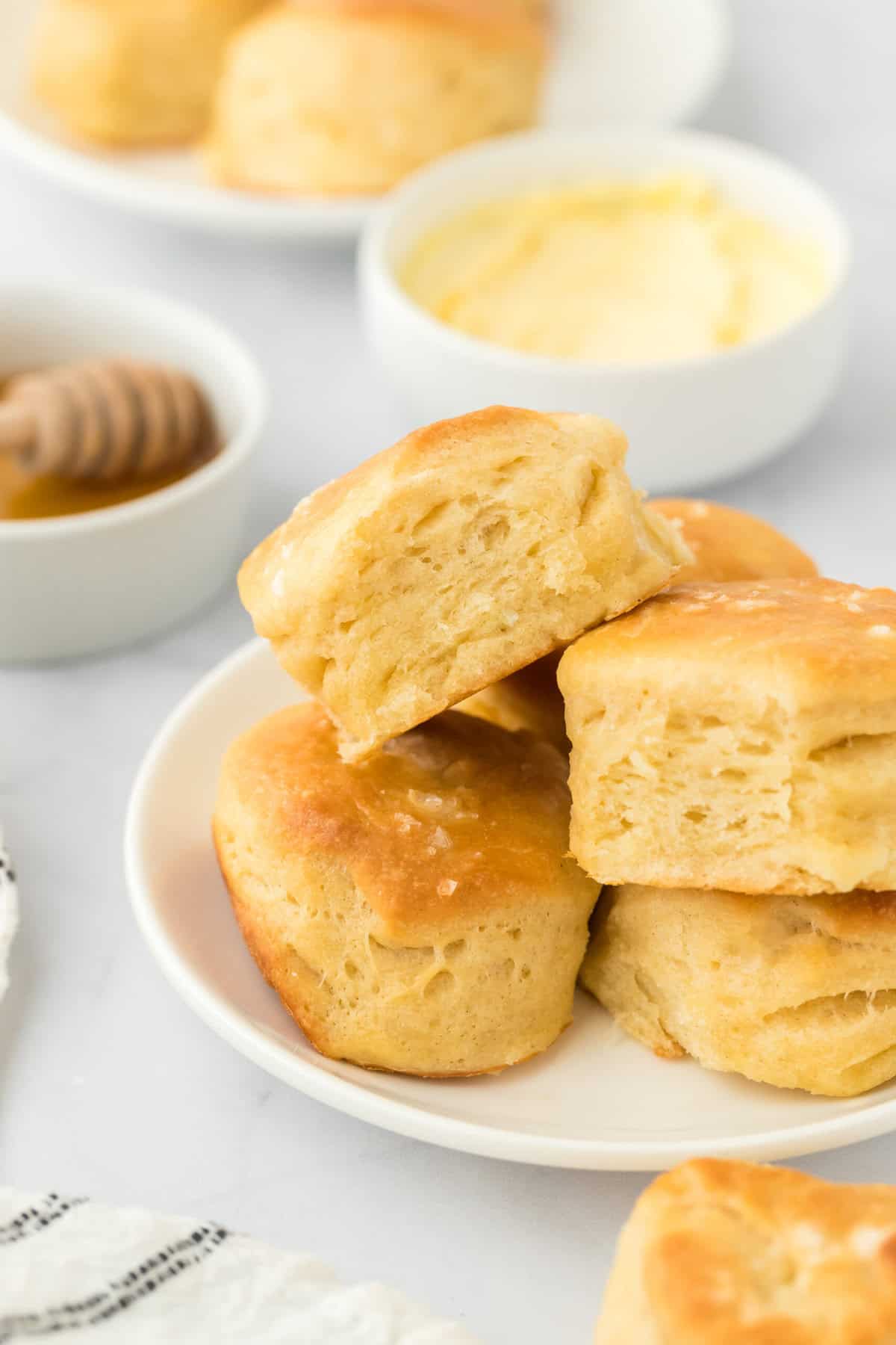 Angel biscuits stacked on top of each other on a white plate with butter in the background