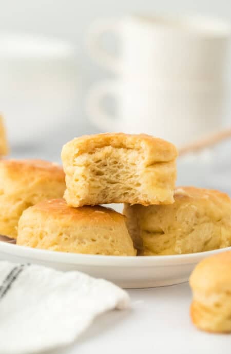 One eaten angel biscuit sitting on top of a pile of biscuits on white backgrorund