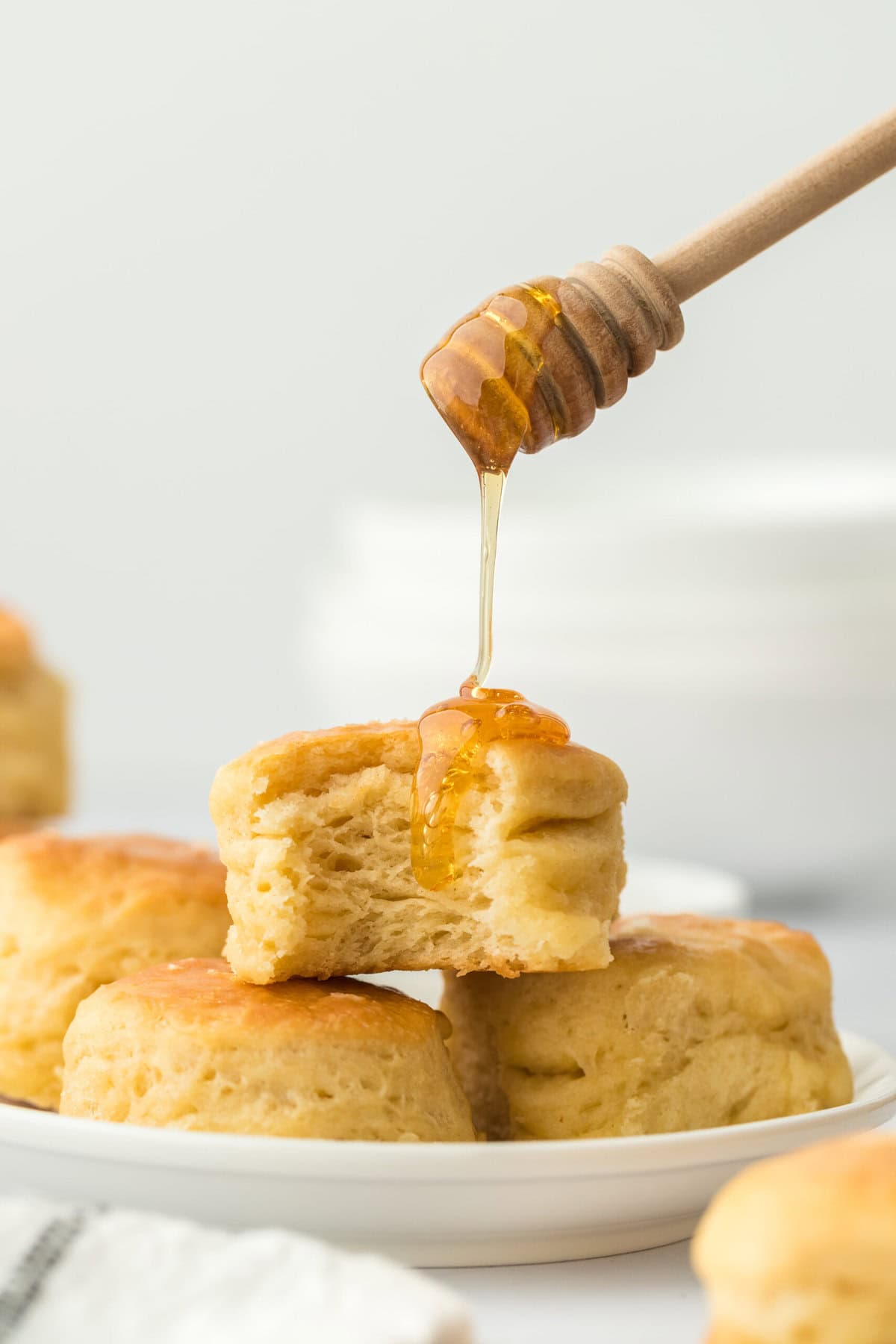 Angel biscuits with honey being drizzled on top on a white plate in a white background